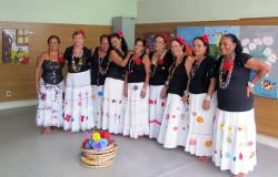 Nove integrantes do Grupo de Cultura Popular Rosas do São Bernardo, com saias coloridas, rosa o cabelo e colares.