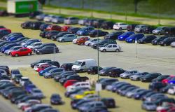Mas de 40 carros estacionados em pátio durante o dia.