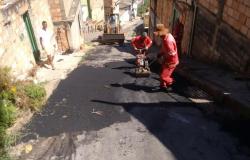 Beco com dois homens trabalhando com material e máquina tapa buracos.