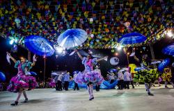 Meninas com vestidos coloridos de quadrilha levantando guarda-chuvas azuis. 