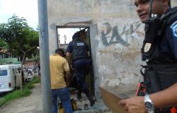Polícia municipal na porta de uma casa abandonada com prancheta na mão, em sua frente estão agentes da prefeitura que então na casa para fazer vistoria de combate a Dengue.