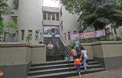 Fachada da Escola Municipal Marconi, que tem uma ampla escadaria, com cinco pessoas entrando e saindo durante o dia.