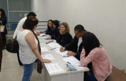 Cinco atendentes em um balcão realizam as inscrições de dois cidadãos na Conferência de Saúde da Regional Oeste.