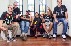 Sete portadores de sofrimento mental que expuseram seus trabalhos estão sentados, reunidos, sorrindo, durante o dia.