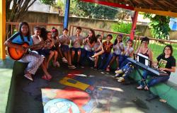 Cerca de 15 pessoas sentadas. Cerca de 10 crianças com instrumentos musicais de sopro e violão.