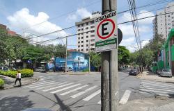 Cruzamento de trânsito com placa de Estacionamento Rotativo em uma das esquinas, durante o dia.