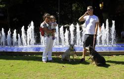 Casal com criança à frente da fonte da Savassi. Criança está no colo da mãe e dois cães encoleirados, presos por guia que está nas mãos do pai. 