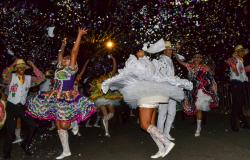 Quadrilha junina com roupas coloridas e mais de cinco membros dança e joga confetes à noite. 