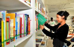 Menina mexe em livro em estante de biblioteca