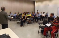 Adultos sentados em sala, assistindo palestra de homem.