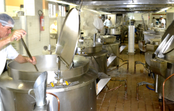 Cozinheiro prepara almoço em panela muito grande de retaurante popular. Ao lado e ao fundo, outras quatro panelas do mesmo tamanho e dois cozinheiros.