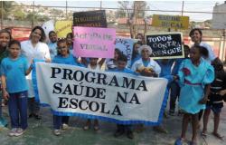 Um grupo de alunos e professores com cerca de dez pessoas empunham cartazes do Programa Saúde na Escola. Foto ilustrativa