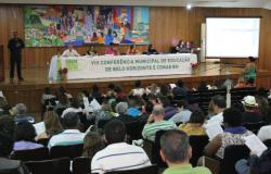 Auditório com cerca de cem pessoas na VIII Conferência Municipal de Educação e Conae- BH. No palco, há uma mesa composta por seis autoridades da educação. Atrás do palco, na parede, vê-se um enorme e colorido painel.
