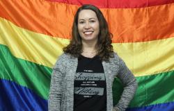 Analista de políticas públicas Elizabeth Matos Marques sorri tendo como fundo bandeira com as cores do arco-íris, símbolo do movimento LGBT.