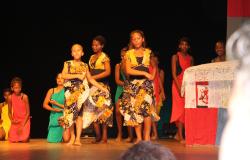 Cerca de 10 crianças em um palco, vestidas com roupas africanas