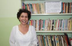 MUlher sorri à frente de estante com livros.