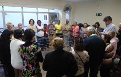 Cerca de catorze idosos em círculo seguram barbantes que formam uma rede, conectando todos as todos.  