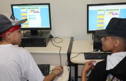 Dois estudantes, cada sentdo um em frente a um computador, se olham. Nas telas, a página do Orçamento Participativo da Criança e do Adolescente  (OPCA). 