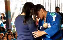 Professor faz demonstração de judô com mulher, assistido por crianças. 