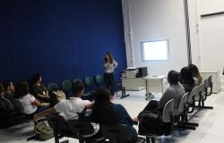 Instrutora, de pé, fala para oito servidores da prefeitura de Belo Horizonte, sentados em meia lua. O ambiente é uma sala fechada. Há cinco cadeiras vazias.