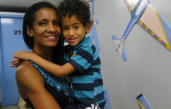 Mãe com filho no colo em Unidade de Saúde, ambos sorridentes.