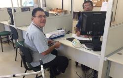 Homem solicita serviços da BHTrans em atendimento presencial; ele está sentado em frente a uma mesa, do outro lado, um homem o atende com computador.