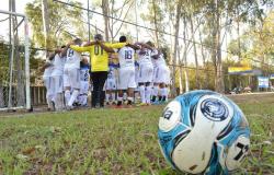 Equipe de futebol reunida no campo antes da partida ao lado da trave, à frente, bola de futebol. 
