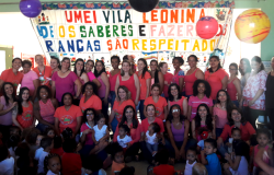 Equipe de cerca de 40 pessoas da Umei Vila Leonida se veste de rosa para conscientizar a todos sobre a importância da prevenção do câncer de mama. Ao fundo, uma grande faixa com os dizeres: UMEI Vila Leonina: onde os saberes e fazeres das crianças dão respeitados.