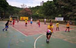 Crianças jogam futebol em quadra. 