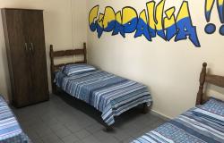 Quarto com três camas e um armário com grafite escrito "cidadania" em uma das paredes