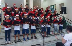 Mais de vinte crianças ensaiam em coral com gorro de Natal. 