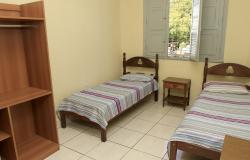 Quarto de unidade de acolhimento institucional para população em situação de rua, com duas camas, uma cabeceira e um armário.