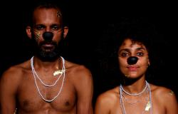 Dois atores negros, homem e mulher, sem camiseta e com nariz de palhaço.