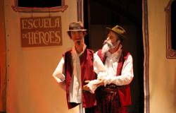 Personagem de peça teatral, Dom Quixote  tem um boneco na mão direita; na parede do cenário ao fundo vê-se uma placa em que está escrito os dizeres "Escola de Heróis".