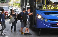 Três estudantes entram em ônibus, seguidos por mulher com sacola de compras, durante o dia.