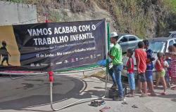 Faixa com os dizeres: "Vamos acabar com o trabalho infantil" é segurada por técnicos da Prefeitura. Ao lado, quatro crianças observam.