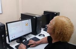 Idosa santada em frente ao computador, digitando