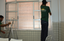 Dois homens instalam tela em janela de centro de saúde.