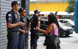 Dois guardas municipais conversam com cidadã na rua, um terceiro guarda observa a rua.